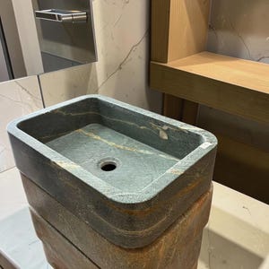 Peut inclure: Un &eacute;vier rectangulaire en pierre, aux tons vert fonc&eacute; et marron. Il pr&eacute;sente un bassin rectangulaire avec un trou d'&eacute;vacuation. L'&eacute;vier est empil&eacute; sur une base en pierre assortie. Id&eacute;al pour une salle de bain.