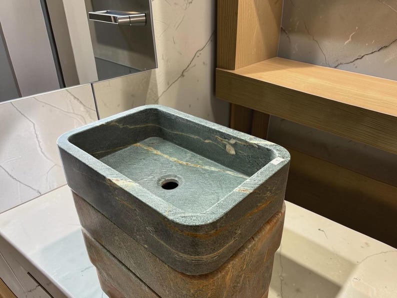 Peut inclure: Un &eacute;vier rectangulaire en pierre, aux tons vert fonc&eacute; et marron. Il pr&eacute;sente un bassin rectangulaire avec un trou d'&eacute;vacuation. L'&eacute;vier est empil&eacute; sur une base en pierre assortie. Id&eacute;al pour une salle de bain.