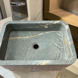 Peut inclure: Un &eacute;vier rectangulaire en pierre, de couleur gris fonc&eacute; et vert. Il pr&eacute;sente un trou d'&eacute;vacuation central et une surface textur&eacute;e avec des stries beiges et marron. Con&ccedil;u pour une utilisation dans la salle de bain.