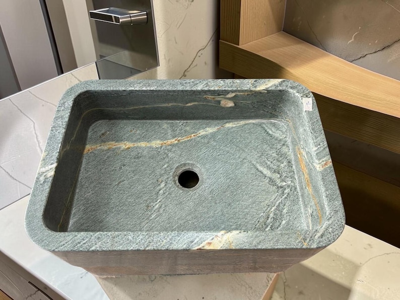 Peut inclure: Un &eacute;vier rectangulaire en pierre, de couleur gris fonc&eacute; et vert. Il pr&eacute;sente un trou d'&eacute;vacuation central et une surface textur&eacute;e avec des stries beiges et marron. Con&ccedil;u pour une utilisation dans la salle de bain.