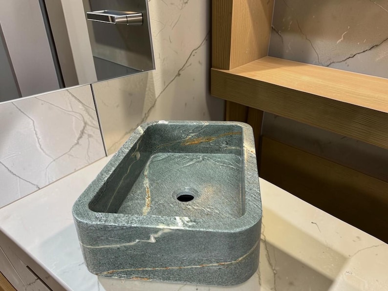 Peut inclure: Un &eacute;vier de salle de bain rectangulaire en pierre aux bords arrondis. L'&eacute;vier est vert mouchet&eacute; avec des stries marron et blanches. L'&eacute;vier a un seul trou d'&eacute;vacuation et est pos&eacute; sur un comptoir blanc.