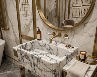 Peut inclure: Une salle de bain luxueuse avec un lavabo en marbre et des accessoires dorés. Le lavabo présente un design cannelé et est associé à un robinet doré et à une quincaillerie assortie. Un miroir rond et des œuvres d'art encadrées sont visibles en arrière-plan.