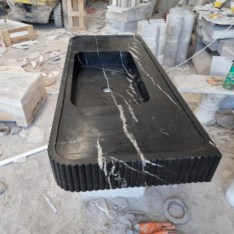 May include: A large, rectangular black marble countertop with a built-in sink basin. The countertop features white veining and a decorative, fluted edge. The sink has a single faucet hole. The countertop is likely for a bathroom or kitchen.