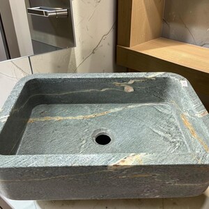 Peut inclure: &Eacute;vier rectangulaire en pierre aux coins arrondis. L'&eacute;vier est de couleur gris-vert mouchet&eacute; avec des stries de beige et de blanc. Il poss&egrave;de un seul trou d'&eacute;vacuation au centre et est con&ccedil;u pour une utilisation dans la salle de bain.