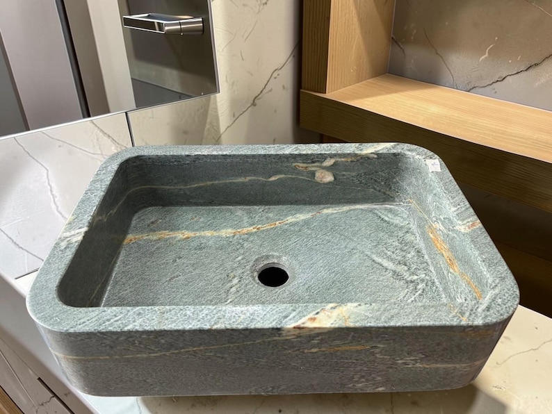 Peut inclure: &Eacute;vier rectangulaire en pierre aux coins arrondis. L'&eacute;vier est de couleur gris-vert mouchet&eacute; avec des stries de beige et de blanc. Il poss&egrave;de un seul trou d'&eacute;vacuation au centre et est con&ccedil;u pour une utilisation dans la salle de bain.