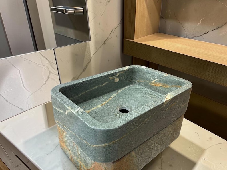 Peut inclure: Un &eacute;vier rectangulaire en pierre, aux tons gris fonc&eacute; et marron. L'&eacute;vier pr&eacute;sente un bassin carr&eacute; et un seul trou d'&eacute;vacuation. Il est fait de pierre en couches et pos&eacute; sur un comptoir blanc.
