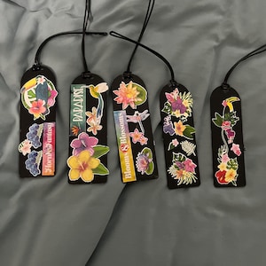 May include: Five black bookmarks with floral designs and black cords. Each bookmark features colorful flower and bird illustrations. Text on the bookmarks includes "Floral Fantasy", "Paradise", and "Blooms & Blossoms".