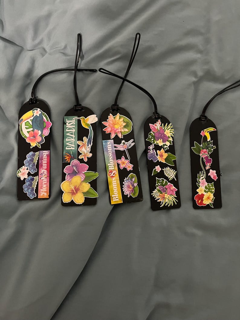 May include: Five black bookmarks with floral designs and black cords. Each bookmark features colorful flower and bird illustrations. Text on the bookmarks includes "Floral Fantasy", "Paradise", and "Blooms & Blossoms".