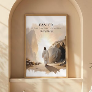 Könnte beinhalten: Gerahmter Kunstdruck mit einer Figur in weißen Gewändern, die zwischen Felsformationen auf ein helles Licht zugeht. Der Text "EASTER IS THE DAY THAT CHANGED everything" ist oben abgebildet. Das Kunstwerk befindet sich in einem goldenen Rahmen.