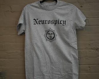 May include: A light gray t-shirt with a black graphic of a sun with a face and the text "Neurospicy" in a gothic font.