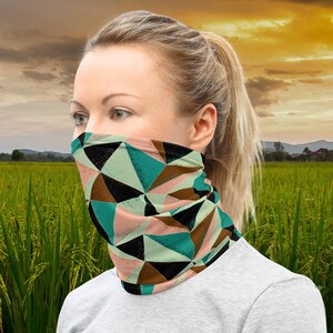 Puede incluir: Una mujer usando una cubierta facial con un patrón geométrico de triángulos negros, marrones, azul verdoso y rosados. El patrón es abstracto y moderno.