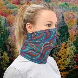 Puede incluir: Una mujer lleva un pasamontañas de color azul verdoso, morado y naranja con un diseño de puntos repetidos. El pasamontañas está hecho de un tejido suave y elástico, perfecto para proteger la cara y el cuello de los elementos.