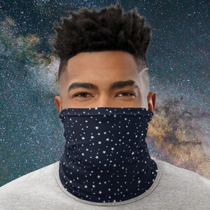 Puede incluir: Un cubrecuello azul marino con un diseño de estrellas blancas. La cubierta facial está hecha de una tela suave y transpirable y está diseñada para usarse alrededor del cuello y subirse sobre la boca y la nariz.