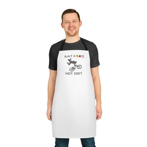 May include: White apron with black adjustable straps. The apron has a graphic of a person riding a bicycle with the text "Eat Food Not Dirt" and a red apple, yellow pear, and orange slice.