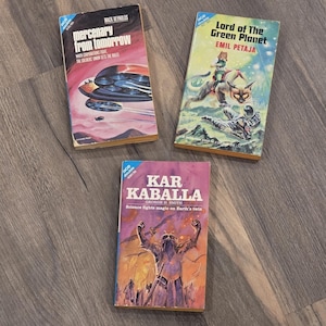 May include: Three vintage science fiction paperback books. Titles include "Mercenary from Tomorrow," "Lord of the Green Planet," and "Kar Kaballa." The covers feature colorful illustrations of spaceships, alien landscapes, and futuristic figures.