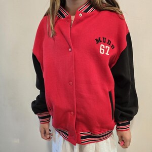 May include: Red and black varsity jacket with the word "Mudd" and the number "67" in white lettering. The jacket has black sleeves, a button-up front, and striped detailing on the cuffs and hem.