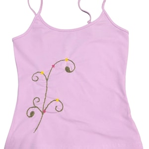 May include: A light purple camisole with thin straps. The camisole features an embroidered design of a brown stem with green, pink, and yellow floral accents. The top is made of a soft material.