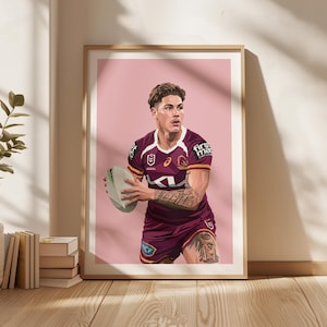 May include: A framed art print featuring a rugby player in a maroon and white jersey, holding a rugby ball. The player has tattoos on his arm and leg. The background is a solid pink colour. The print is in a wooden frame.