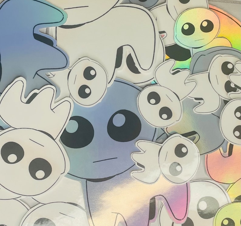 May include: A collection of colorful, cartoon-style stickers featuring various characters with large eyes and simple designs. The stickers are printed on white paper and have a glossy finish.