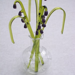 May include: A glass vase with a round body and a narrow neck holds a bouquet of green glass flowers with purple glass buds.