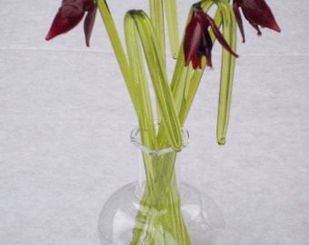 May include: A glass vase with a round base and a narrow neck holds a bouquet of five glass flowers. The flowers are green and red, with the red flowers resembling tulips.