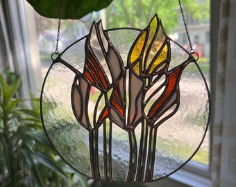 May include: A stained glass window hanging from a chain. The window is round and features three stylised tulips in shades of white, yellow, orange, and brown.