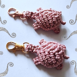 Può includere: Due portachiavi a forma di tartaruga in crochet rosa con anelli in metallo dorato. Le tartarughe sono fatte di filo e hanno una superficie testurizzata.