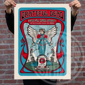 May include: A vintage poster featuring the words "Grateful Dead" in a red, stylized font. The poster includes an illustration of a woman with angel wings, skeletons, and the text "Barton Hall, Cornell University, 117 Statler Dr. Ithaca, NY 14853" and "8 MAY 1977".