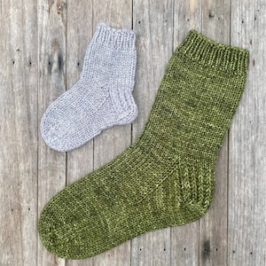 Puede incluir: Dos pares de calcetines de punto, uno de color gris claro y el otro de color verde oscuro. Los calcetines están colocados sobre una superficie de madera.