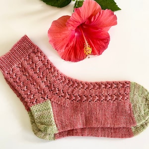 May include: A pair of knitted socks in a pink and green color scheme. The socks have a lacy pattern and are folded over.