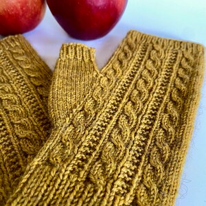 Könnte beinhalten: Ein Paar fingerlose Strickhandschuhe in Senfgelb mit einem Zopfmuster.