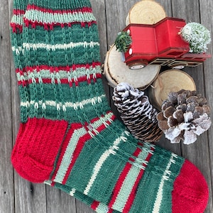 Könnte beinhalten: Ein Paar gestrickte Socken in Grün, Rot und Weiß mit roter Ferse und Spitze. Die Socken liegen auf einer Holzoberfläche.