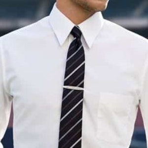 May include: A white long-sleeve dress shirt with a black and white striped tie. The tie has a silver tie bar.