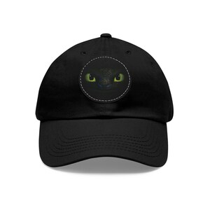 May include: Black baseball cap with a circular patch featuring a close-up of a dragon's face with green eyes.