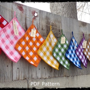 Puede incluir: Una colección de paños de cocina de ganchillo de colores colgados en una valla de madera. Los paños de cocina están hechos en un patrón de cuadros vichy con diferentes combinaciones de colores, incluyendo rojo y blanco, rosa y blanco, naranja y blanco, amarillo y blanco, verde y blanco, azul y blanco, morado y blanco, marrón y blanco y negro y blanco. Los paños de cocina están etiquetados con etiquetas escritas a mano. El texto "PDF Pattern" es visible en la parte inferior de la imagen.