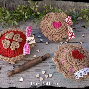 May include: Three crocheted heart-shaped pies made with red and brown yarn. The pies are decorated with lace and ribbon. The pies are labelled "Sugar", "Cutie", and "Love You".