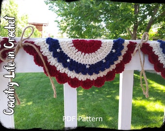 May include: A crocheted American flag bunting with red, white, and blue yarn. The bunting is strung with twine and hangs on a white picket fence. The text "Country Life in Crochet" and "PDF Pattern" is visible in the image.