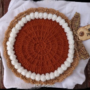 Könnte beinhalten: Gehäkelter Süßkartoffel-Kuchen mit braunem Teig, weißer Sahne und orangefarbener Füllung. Ein Etikett mit der Aufschrift "Sweet Potato" ist mit einem karierten Band befestigt. Der Text "Country Life in Crochet" ist sichtbar.