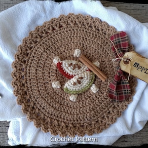 May include: Crochet pattern for a brown apple-themed coaster with cinnamon sticks and a red and black plaid bow. The pattern is called "Country Life in Crochet".