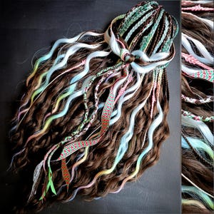 May include: A collection of brown, wavy synthetic dreadlocks with strands of light blue, pink, green, and yellow. Braided accents and decorative ribbons in various colors are intertwined throughout the hair, creating a vibrant and unique style.