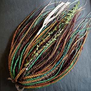 May include: A collection of colorful dreadlocks in shades of brown, green, and gold, adorned with white lace and faux greenery. The dreadlocks are braided and styled, creating a bohemian aesthetic.