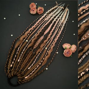 May include: A set of brown, pink, and white dreadlocks with decorative accents. The dreadlocks are arranged on a black surface with faux pearls and pink flowers. The dreadlocks are styled with braids and wavy sections.