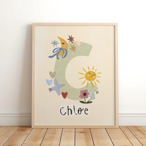 May include: A framed wall art print featuring a large, light green letter C decorated with a yellow crescent moon, a smiling sun, stars, hearts, a blue bird, and flowers. The name Chloe is printed in black, handwritten-style letters below the C.