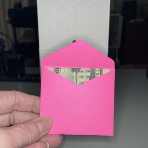 May include: A pink envelope with a dollar bill peeking out from the top.