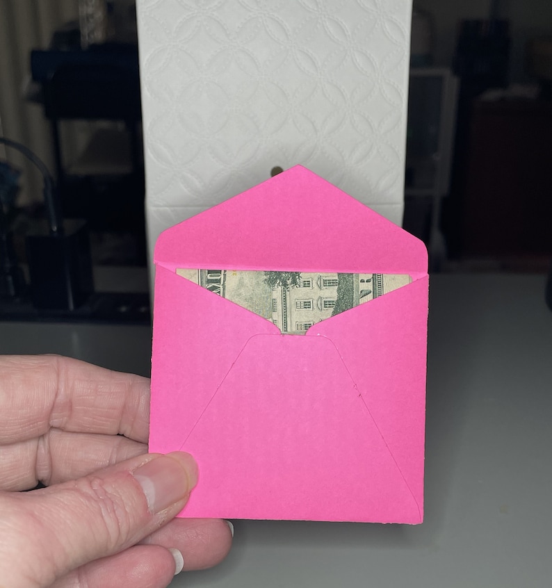 May include: A pink envelope with a dollar bill peeking out from the top.