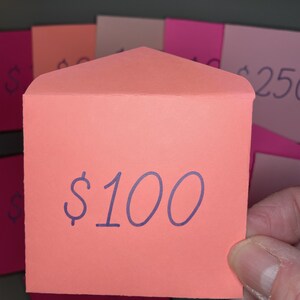 May include: A bright orange envelope with a folded flap. The envelope has the text "$100" written in purple ink.