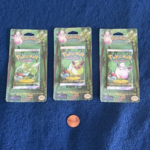 Peut inclure: Trois paquets scellés de boosters du jeu de cartes à collectionner Pokémon. Chaque paquet présente un personnage Pokémon différent sur le devant : un Pokémon de la jungle vert et jaune, un Eevee brun et blanc et un Rondoudou blanc et rose. Chaque paquet contient 11 cartes de jeu supplémentaires.