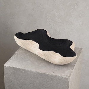 Op de afbeelding: Een decoratieve houten kom met een natuurlijke houten buitenkant en een zwart interieur. De kom heeft een organische vorm en staat op een betonnen blok. De houtnerf is aan de buitenkant zichtbaar. Afmetingen: ongeveer 30 cm lang.