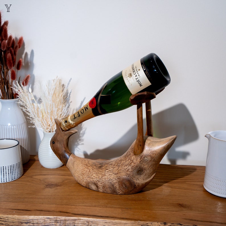 Pu&ograve; includere: Porta bottiglie di vino in legno a forma di uccello con una bottiglia di champagne Mo&euml;t & Chandon appoggiata su di esso. La bottiglia &egrave; inclinata, come se l'uccello stesse bevendo da essa.