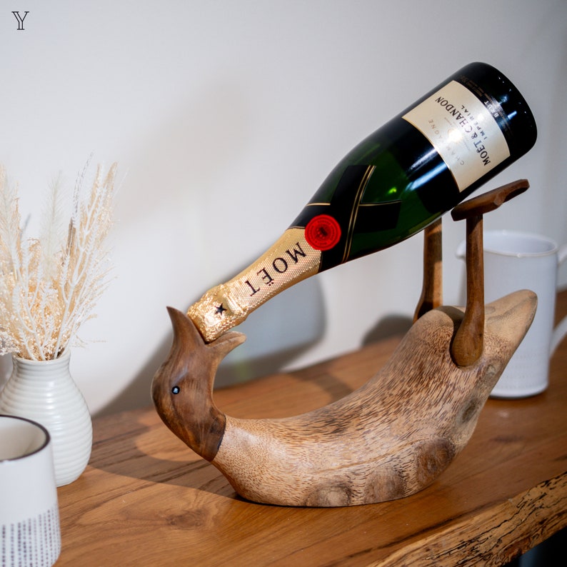 Pu&ograve; includere: Un porta bottiglie di legno a forma di uccello con una bottiglia di champagne Mo&euml;t & Chandon in vetro verde che riposa al suo interno. La bottiglia &egrave; inclinata, con il collo della bottiglia che poggia sul becco dell'uccello.
